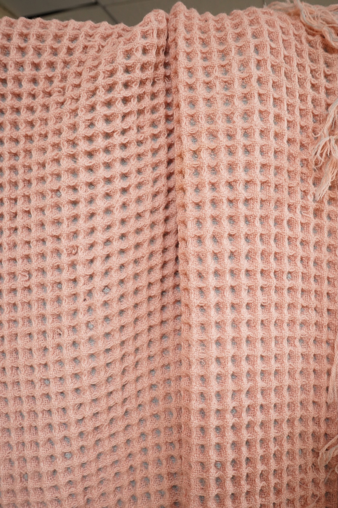 A pink and grey Welsh blanket with tasseled edges